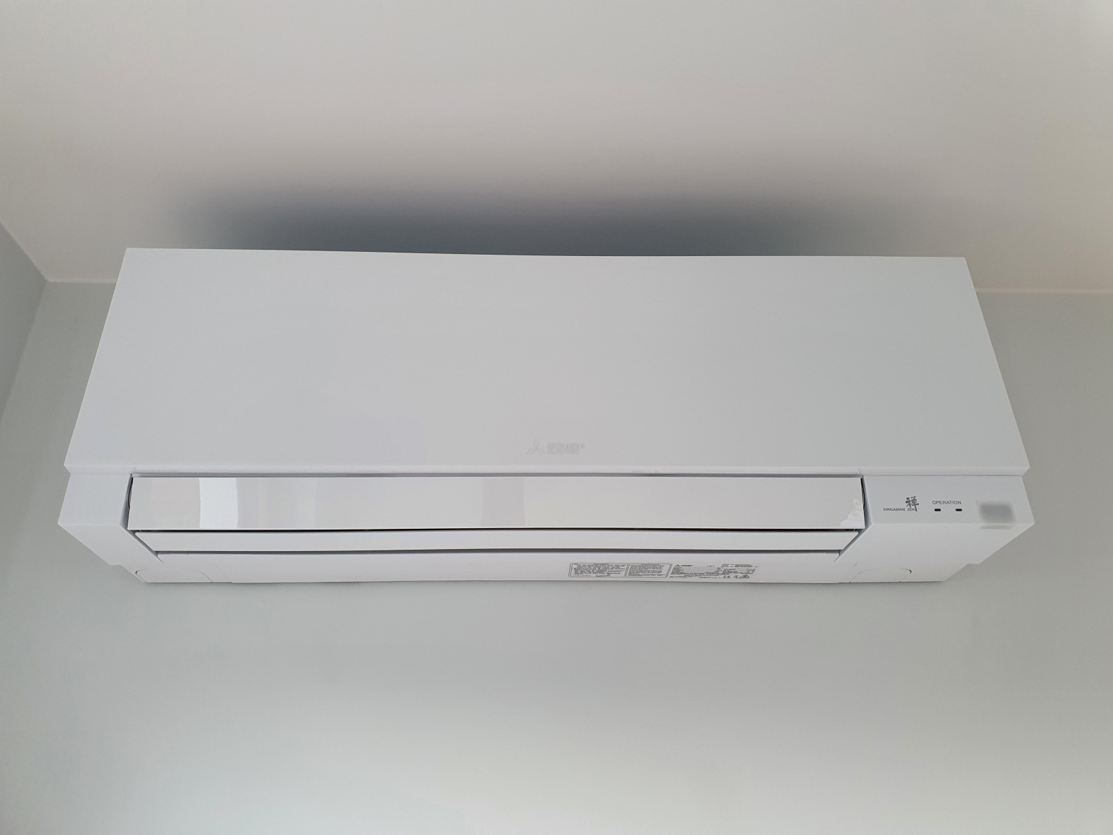 Biała jednostka wewnętrzna klimatyzatora Mitsubishi Electric MSZ-EF Premium zamontowana na jasnoszarej ścianie, widok z dołu.