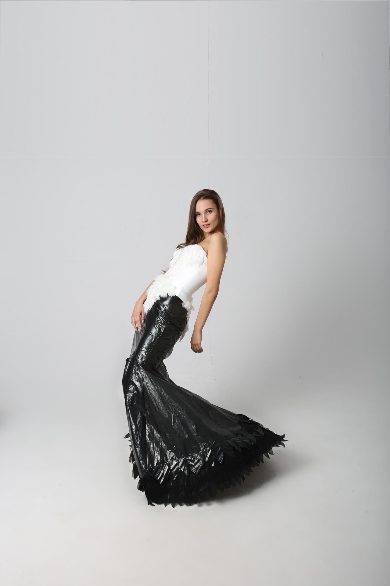 Kobieta w oryginalnej kreacji: biały gorset z piórami i długa czarna spódnica z folii, pozuje w studio w Warszawie.