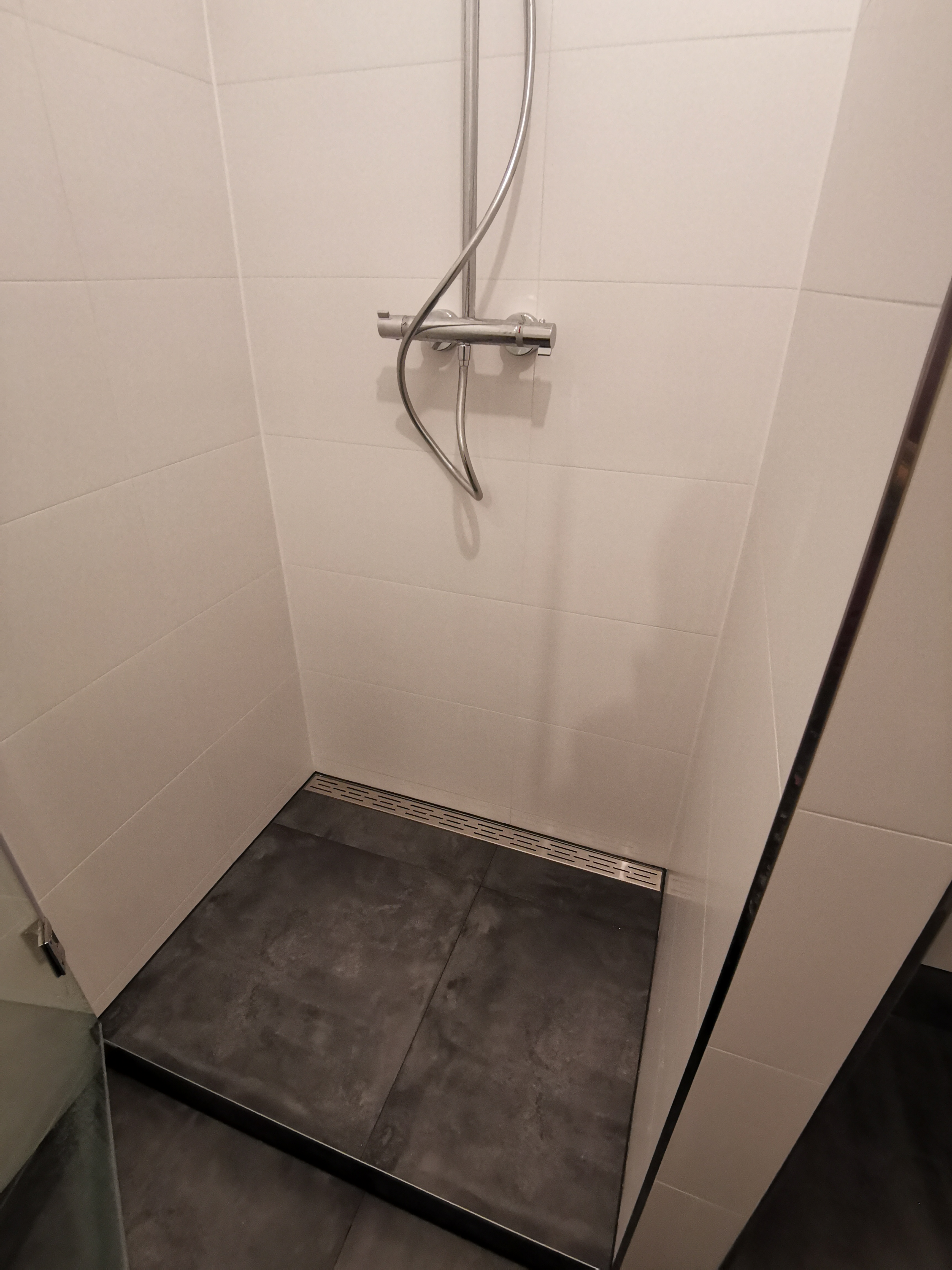 Kabina prysznicowa z odpływem liniowym, wykończona białymi płytkami ściennymi i ciemnymi płytkami podłogowymi.