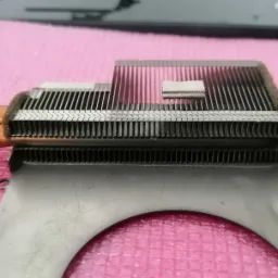 Miedziany radiator z ciepłowodami i aluminiowymi żeberkami, widoczne ślady pasty termoprzewodzącej, leżący na różowej macie antystatycznej.