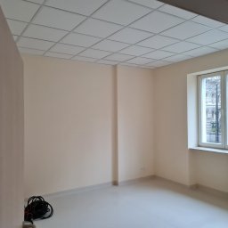 Pol-Ros - Pusty, świeżo pomalowany pokój z kasetonowym sufitem, widokiem na ulicę przez okno i kable na podłodze w rogu.