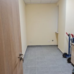 Pol-Ros - Puste pomieszczenie biurowe z szarą podłogą z płytek, świeżo pomalowanymi ścianami w odcieniach beżu, z otwartymi drzwiami z drewnianą okleiną i wózkiem transportowym z tyłu.