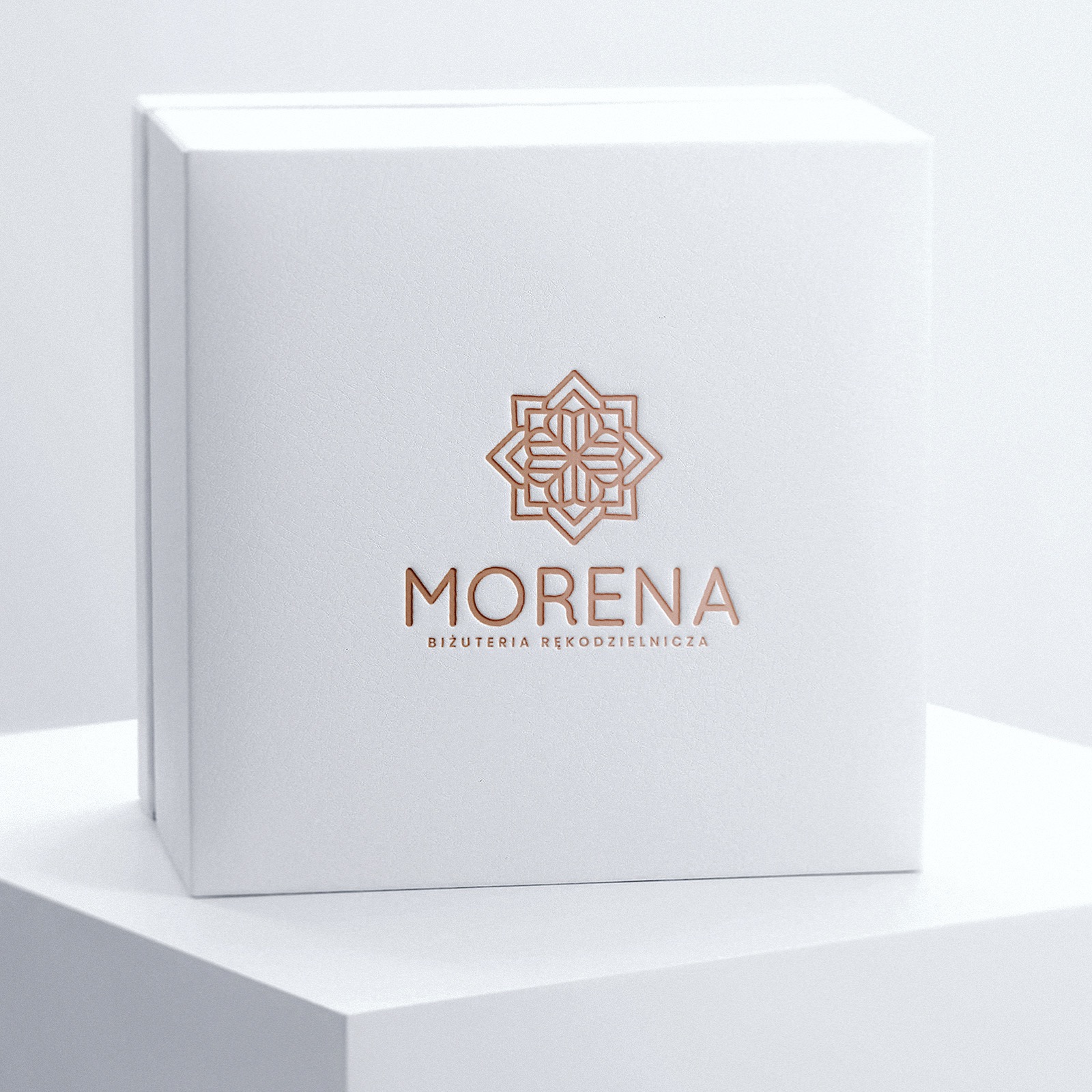 Białe pudełko z tłoczonym złotym logo i napisem 'MORENA Biżuteria Rękodzielnicza' na minimalistycznym, białym tle.