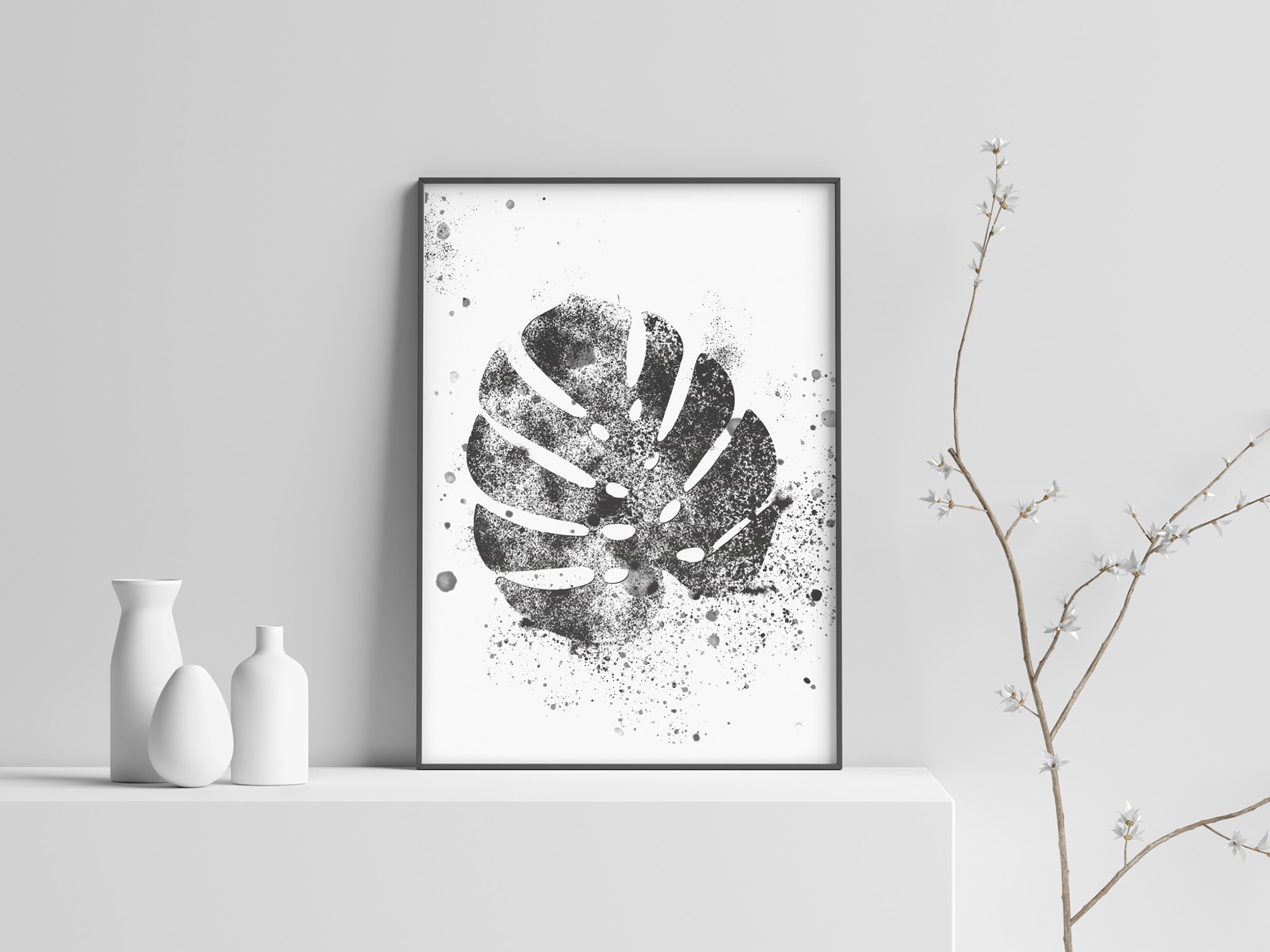 Minimalistyczna grafika monstery w czarnej ramie, umieszczona na białej półce obok białych wazonów i gałązki z drobnymi kwiatami, na tle jasnoszarej ściany.