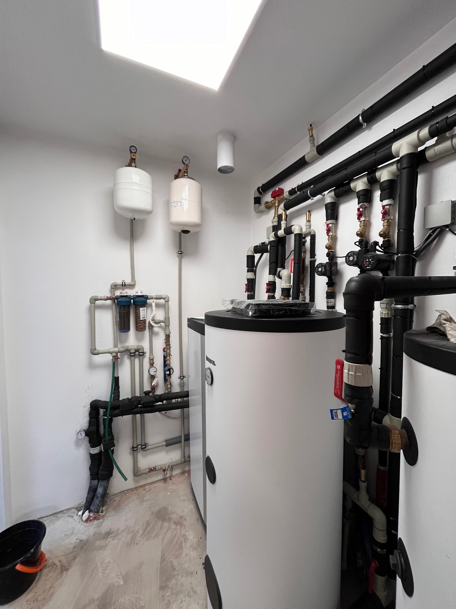 Złożona instalacja hydrauliczna z dwoma zbiornikami buforowymi i filtrami w Sochaczewie. Różnorodne rury i zawory tworzą skomplikowany system w pomieszczeniu technicznym.