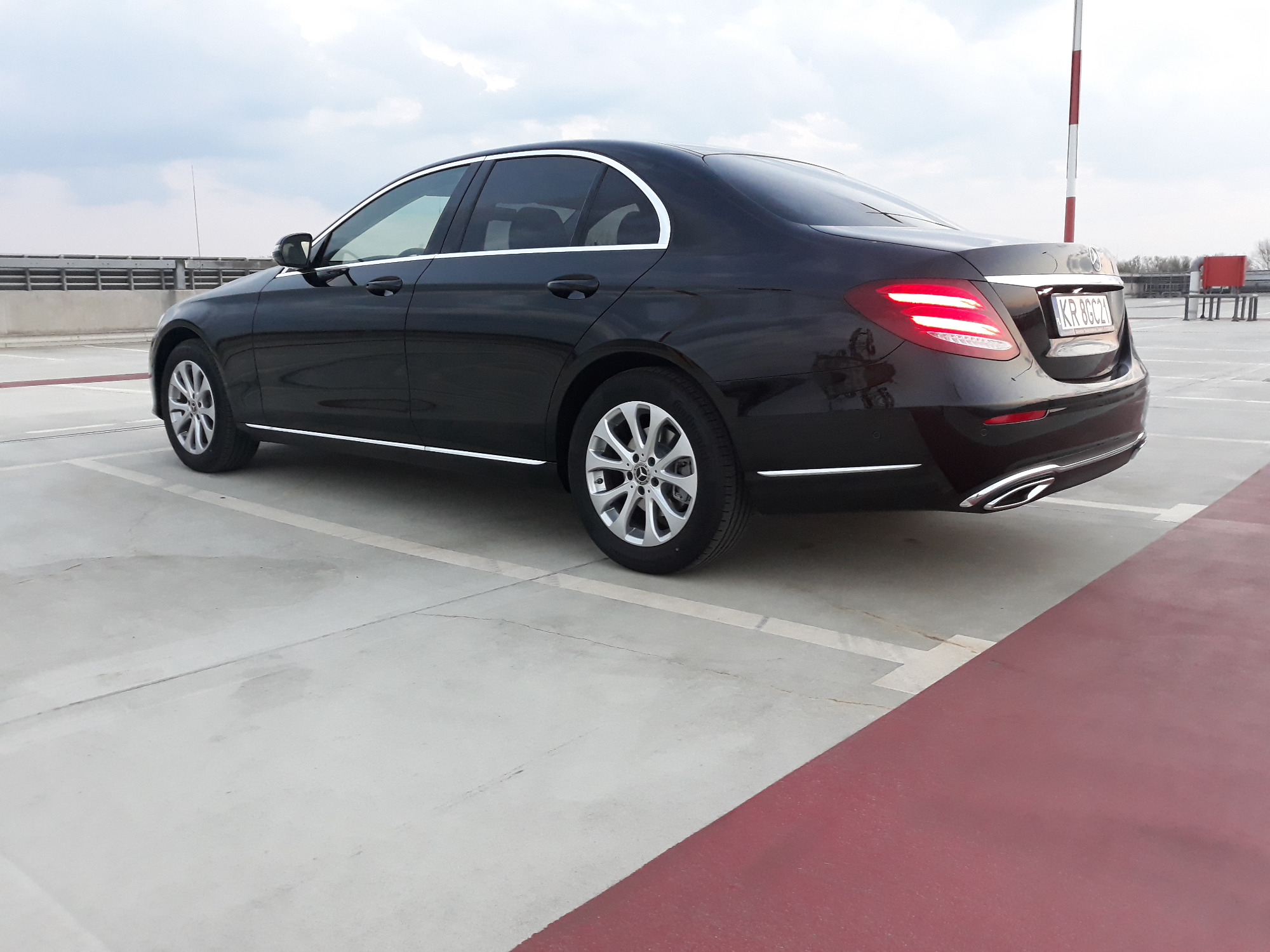 Czarny sedan Mercedes-Benz zaparkowany na betonowym parkingu, widok z tyłu i boku, z włączonymi światłami stopu.