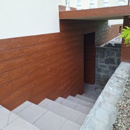 Pro-line - Zewnętrzne schody prowadzące do piwnicy z elewacją imitującą drewno i kamienne fundamenty.