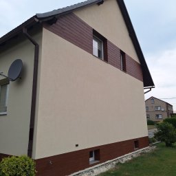 Pro-line - Wykończona elewacja domu jednorodzinnego z brązowym pasem imitującym drewno, widoczne okna i antena satelitarna, trawnik przed budynkiem.