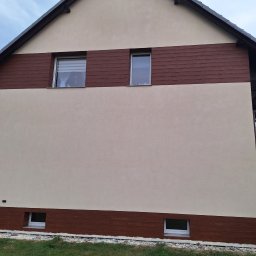 Pro-line - Dwukondygnacyjny dom z beżową elewacją i poziomymi panelami imitującymi drewno, widoczne okna z roletami w górnej części i małe okienka przy gruncie, trawnik z przodu.