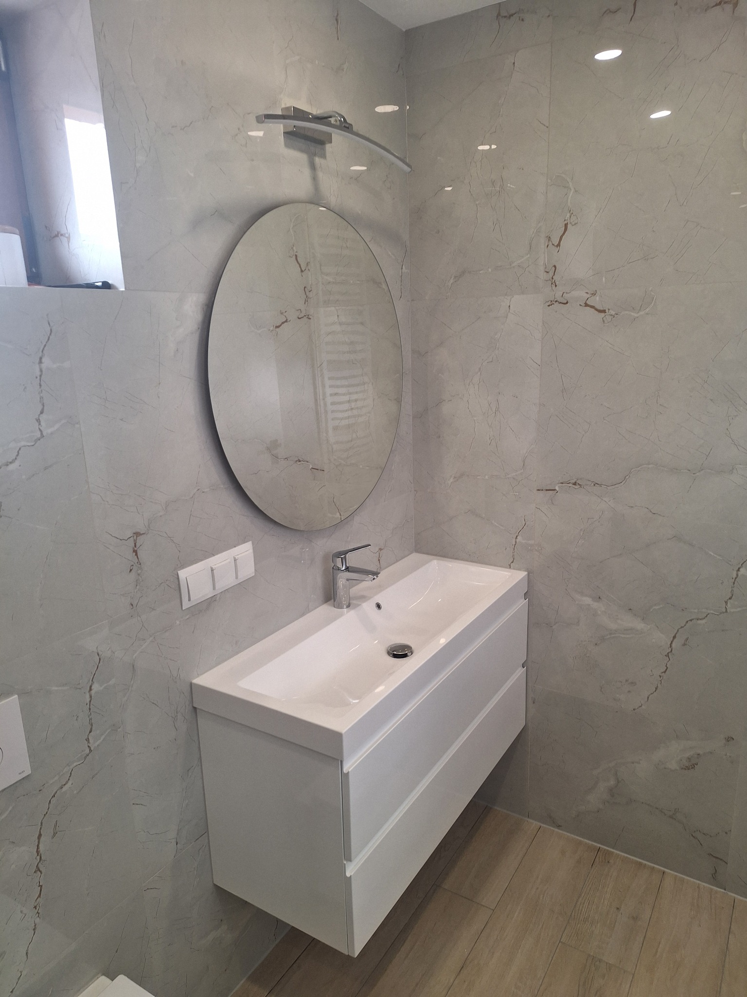 Nowoczesna łazienka z umywalką nablatową na szafce, okrągłym lustrem i marmurowymi płytkami ściennymi.