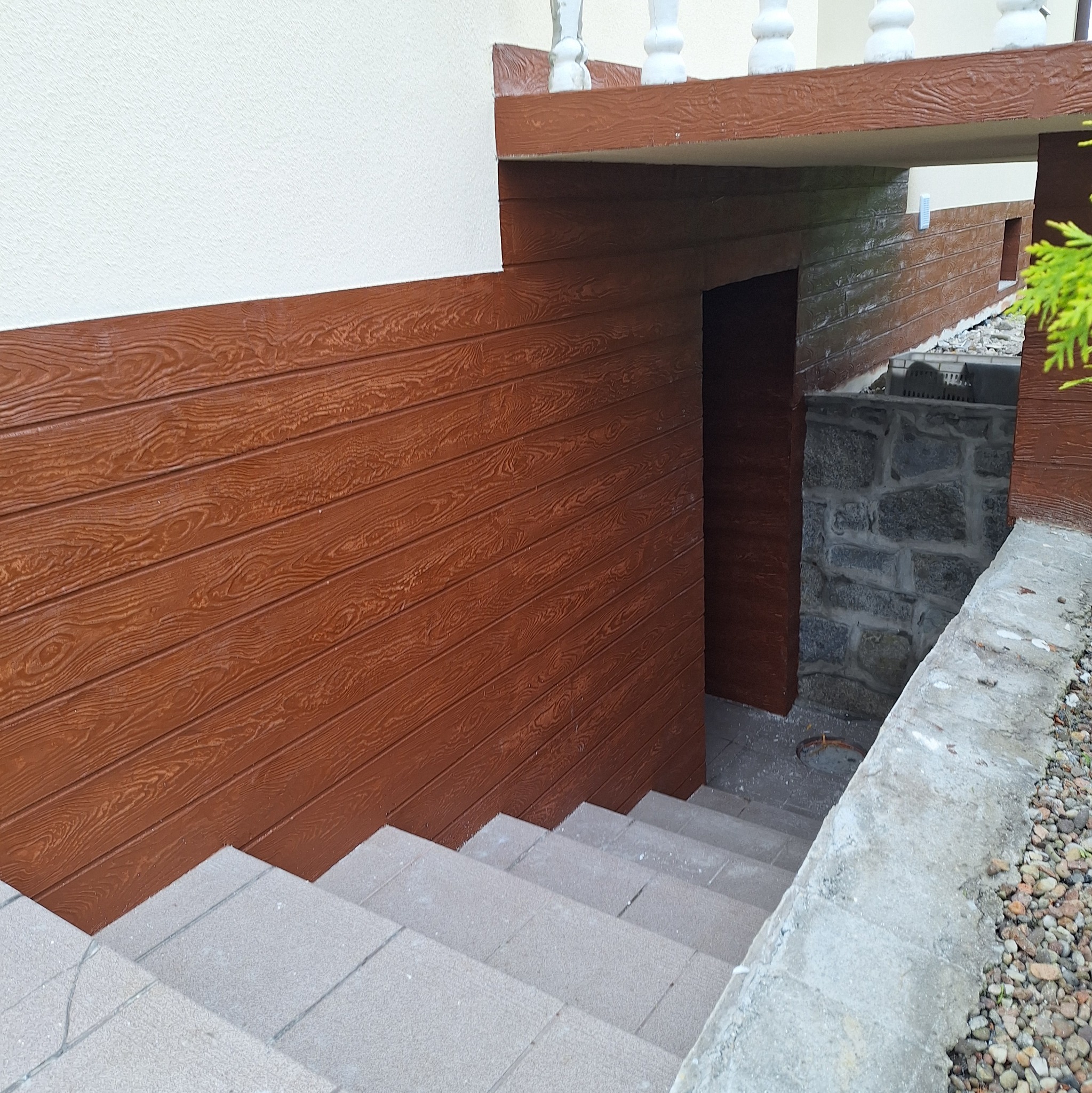 Zewnętrzne schody prowadzące do piwnicy z elewacją imitującą drewno i kamienne fundamenty.