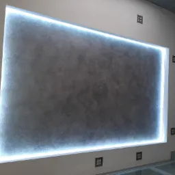 Dekoracyjna ściana z szarą fakturą, podświetlona listwą LED, z widocznymi gniazdkami w stylu retro i fragmentem szklanej podłogi.