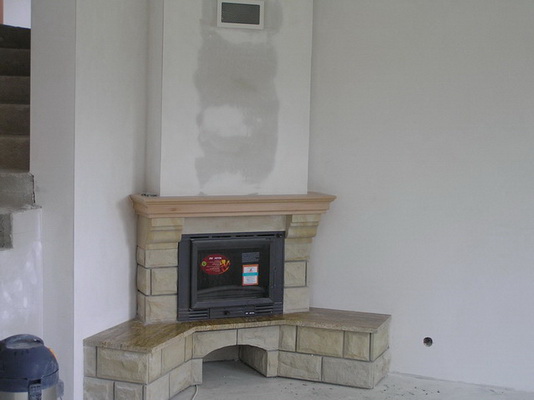 Nowoczesny kominek obudowany kamieniem piaskowca z drewnianym blatem, jeszcze przed malowaniem ścian i wykończeniem podłogi.