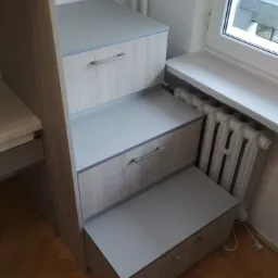 Schody z szufladami na wymiar, zintegrowane z meblem, obok okna i grzejnika, drewniana podłoga.