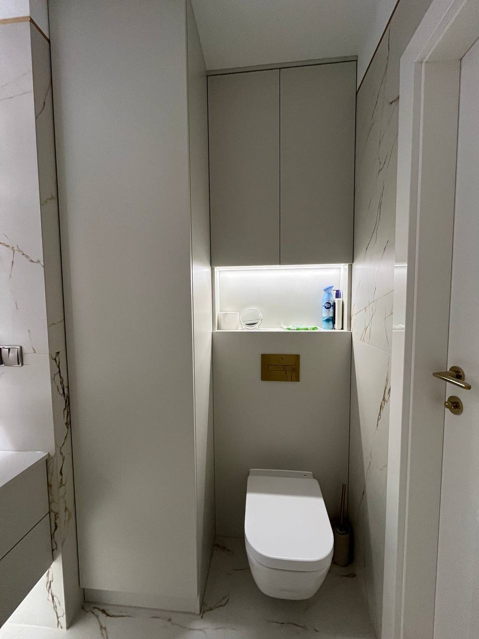 Nowoczesna łazienka z zabudową meblową w odcieniach szarości, podwieszana toaleta, marmurowe płytki z złotymi żyłami i oświetlenie LED.