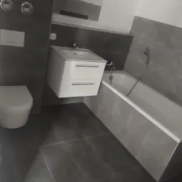 Nowoczesna łazienka z szarymi płytkami, podwieszaną szafką z umywalką i białą wanną.