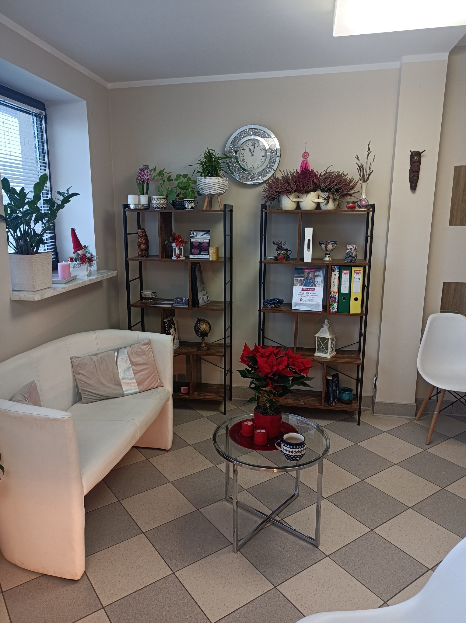 Jasne wnętrze biura z sofą, regałami z dekoracjami i stolikiem kawowym z poinsecją i filiżanką.