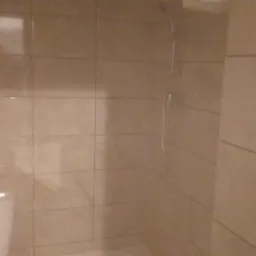 Wykończona łazienka z beżowymi płytkami, widoczny biały sedes i kabina prysznicowa z chromowaną słuchawką.