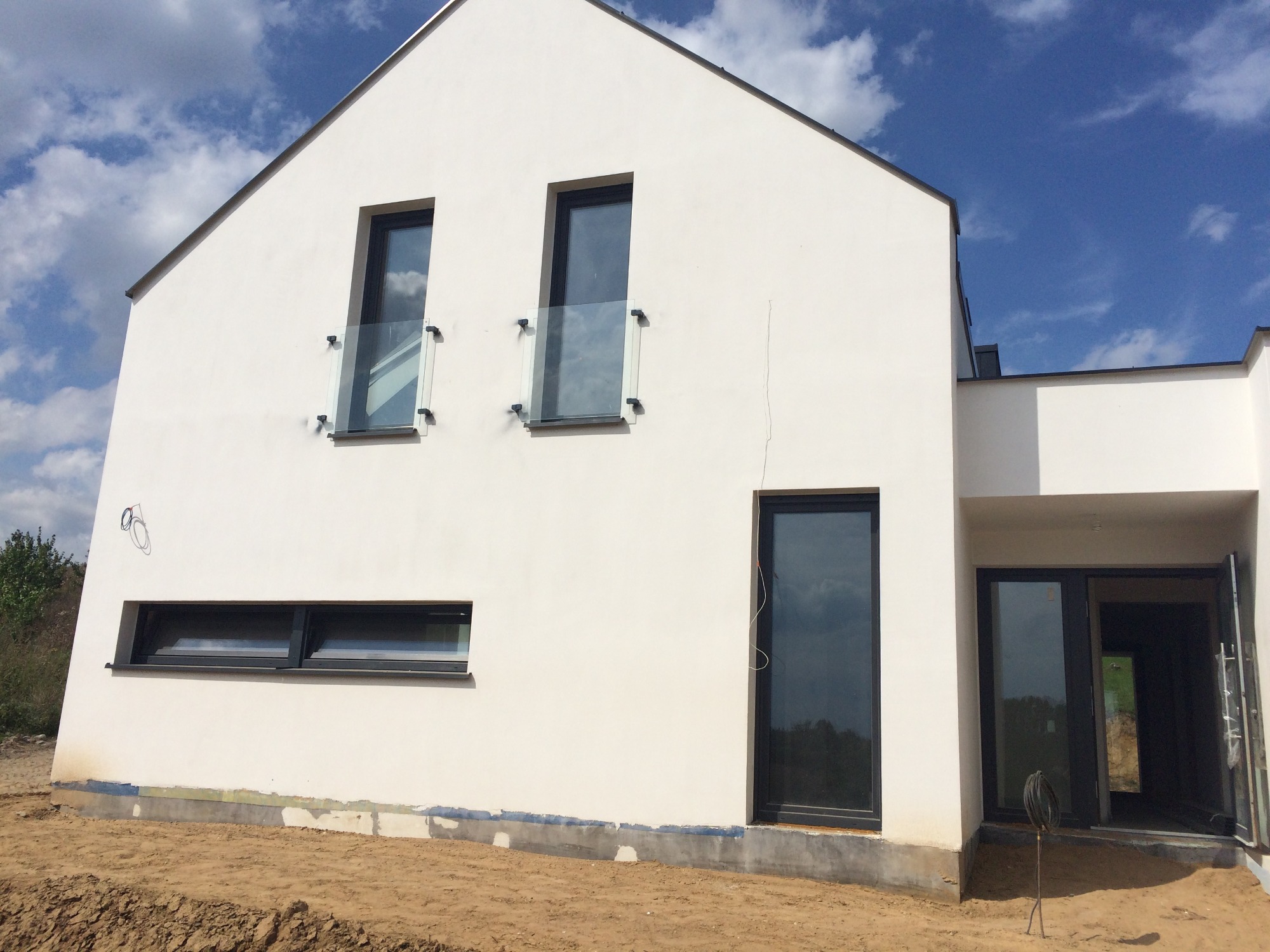 Nowoczesny, biały dom jednorodzinny z ciemnymi oknami i przeszklonymi balustradami, widok z zewnątrz na tle błękitnego nieba z chmurami.