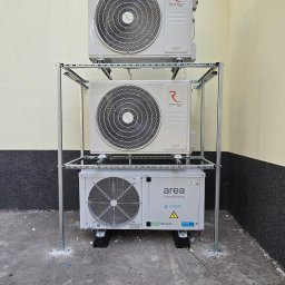 Klimatyka.com Bartłomiej Szrejner - Trzy jednostki zewnętrzne klimatyzacji zamontowane jedna nad drugą na metalowej konstrukcji wsporczej przy ścianie budynku. Dwie górne jednostki marki Rotenso, dolna marki Area.