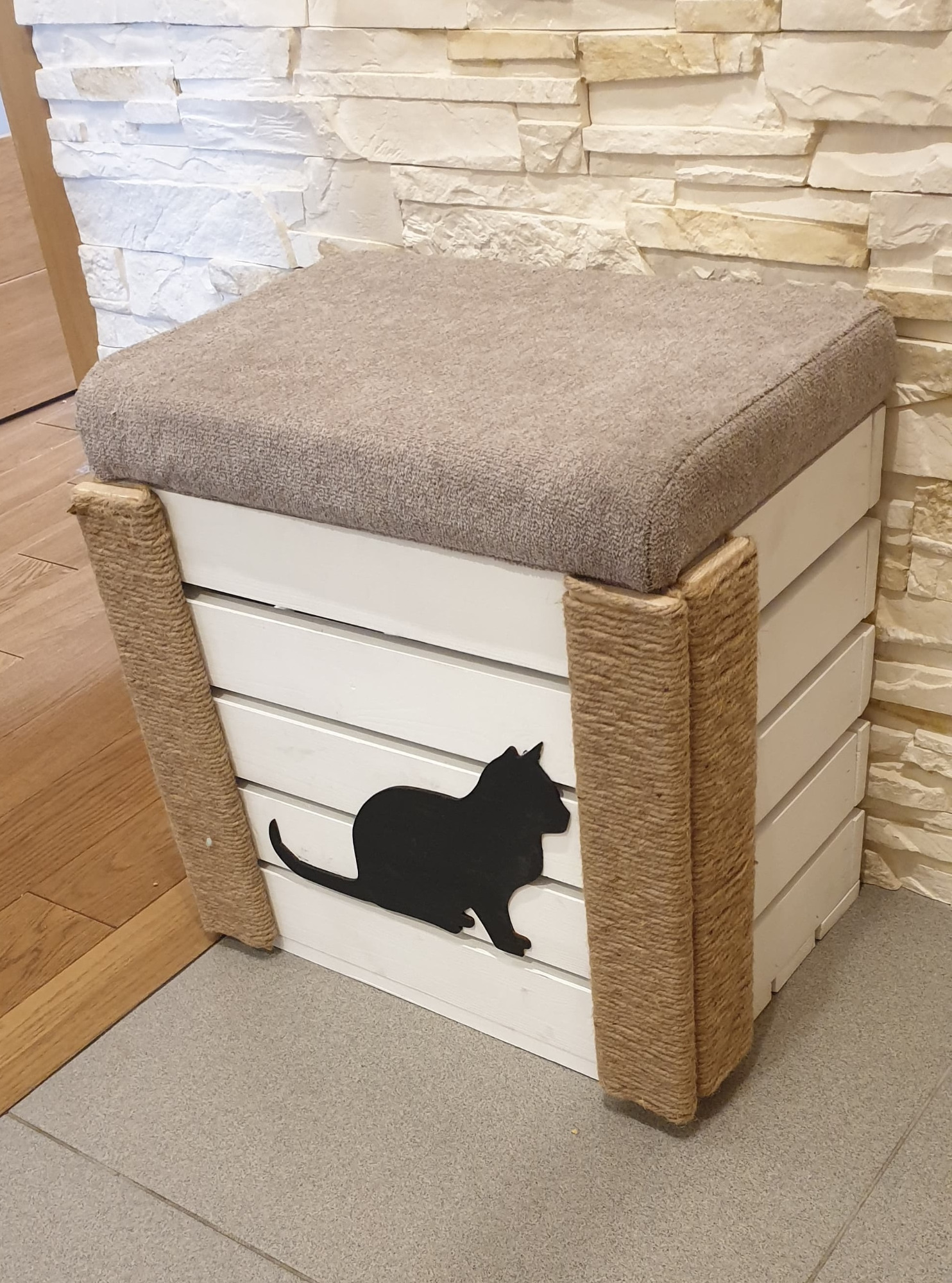 Biały puf ze szczebelków z szarym siedziskiem, ozdobiony jutowym sznurkiem na rogach i czarną sylwetką kota.