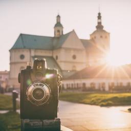 Spółka Rzeszowska - Czarno-biały aparat fotograficzny Filmbox na pierwszym planie, w tle rozmyty kościół w promieniach zachodzącego słońca.