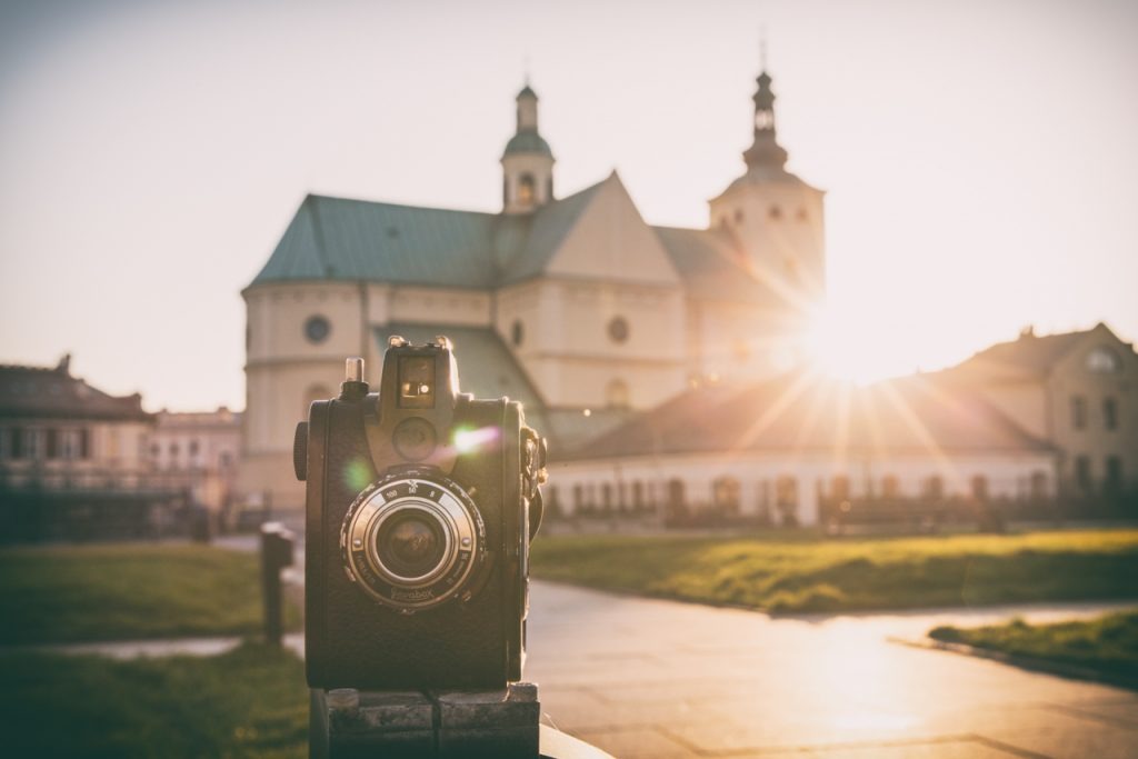Czarno-biały aparat fotograficzny Filmbox na pierwszym planie, w tle rozmyty kościół w promieniach zachodzącego słońca.