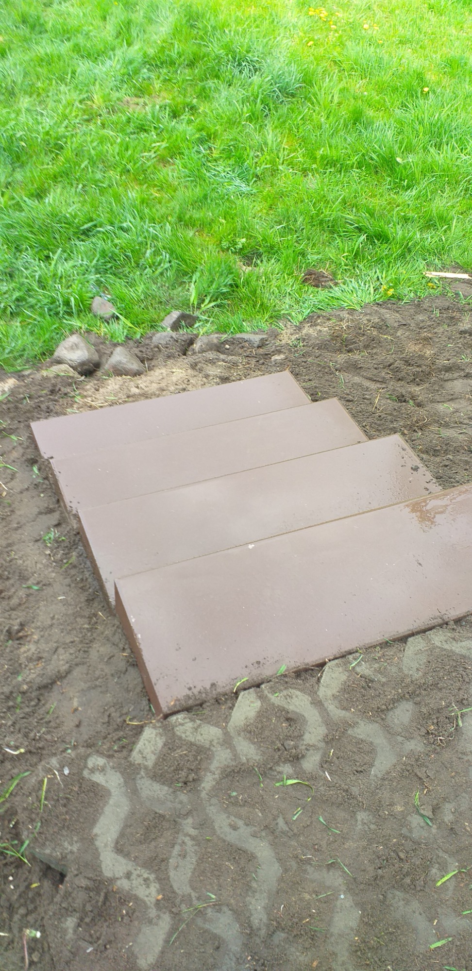 Schody z płyt brukowych w trakcie budowy na trawniku, widoczne ślady po układaniu kostki brukowej.