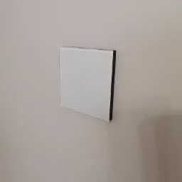 Szklany, dotykowy włącznik światła z czerwoną obwódką na beżowej ścianie, zamontowany na wysokości wzroku.