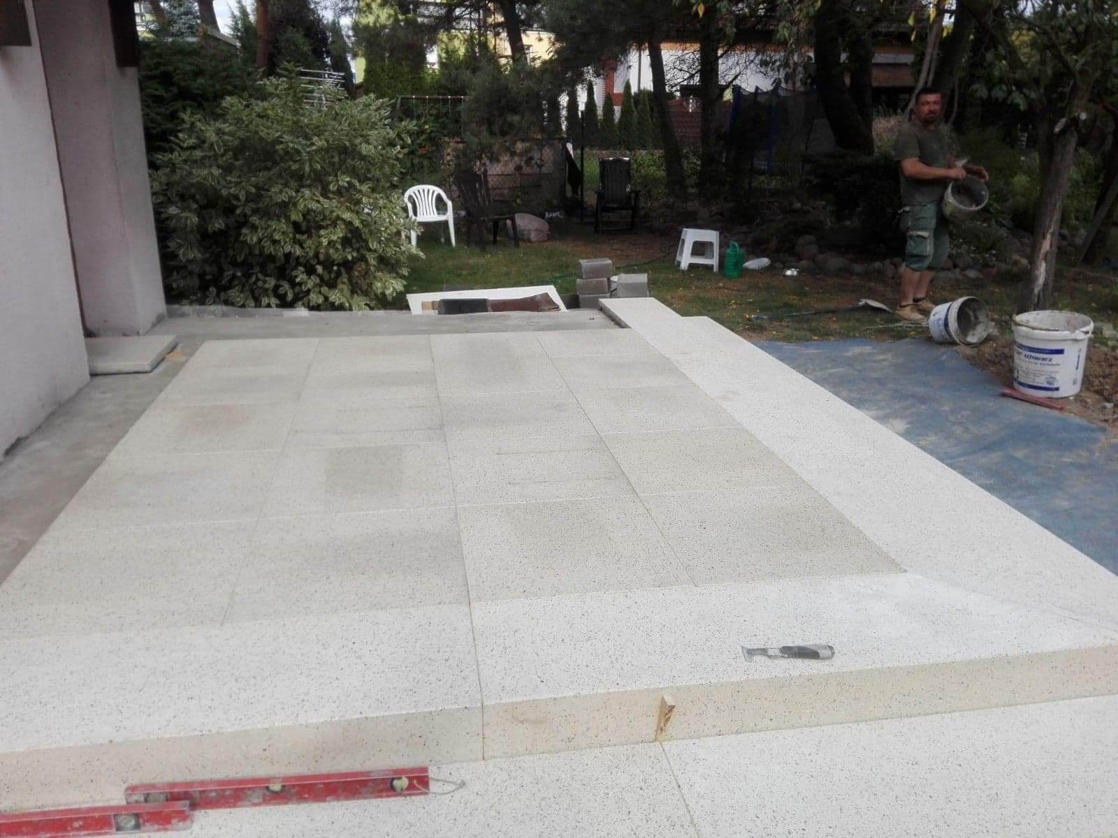 Montaż jasnej kostki na tarasie z widocznym poziomem i pracownikiem z wiadrem w tle.