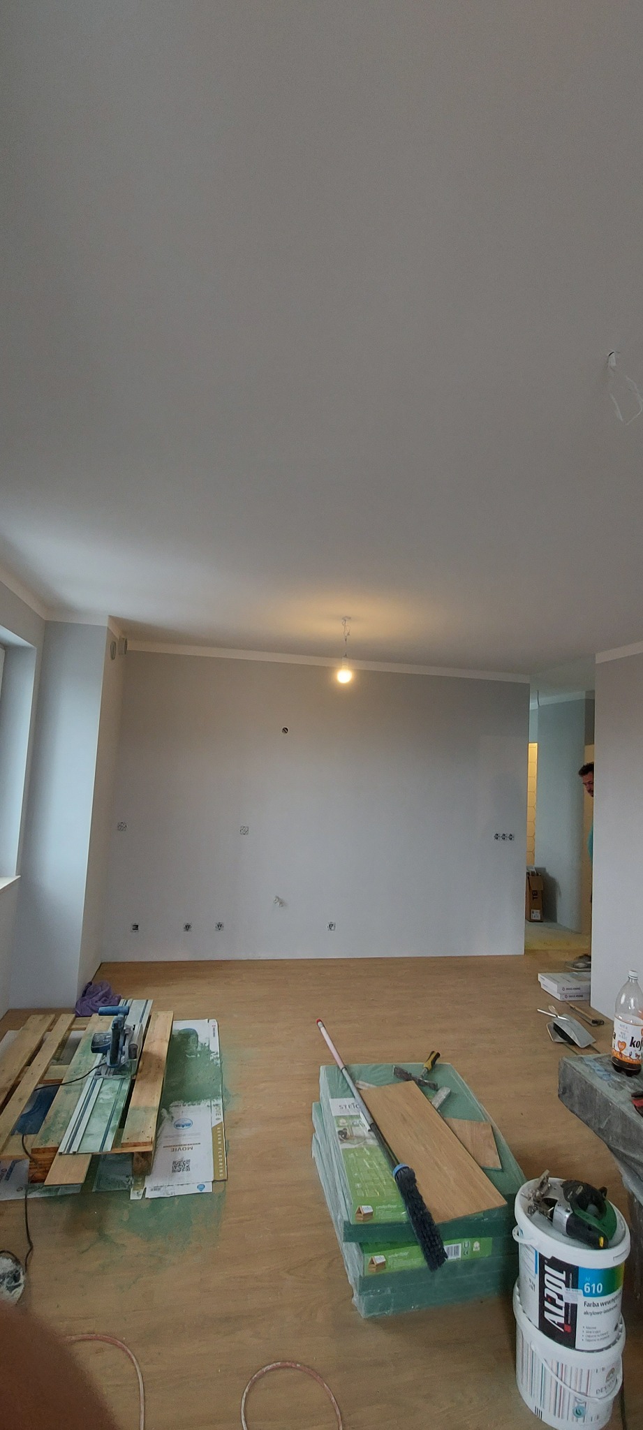Wnętrze pokoju w trakcie prac wykończeniowych: położona podłoga, ściany przygotowane pod malowanie, widoczne narzędzia i materiały budowlane.