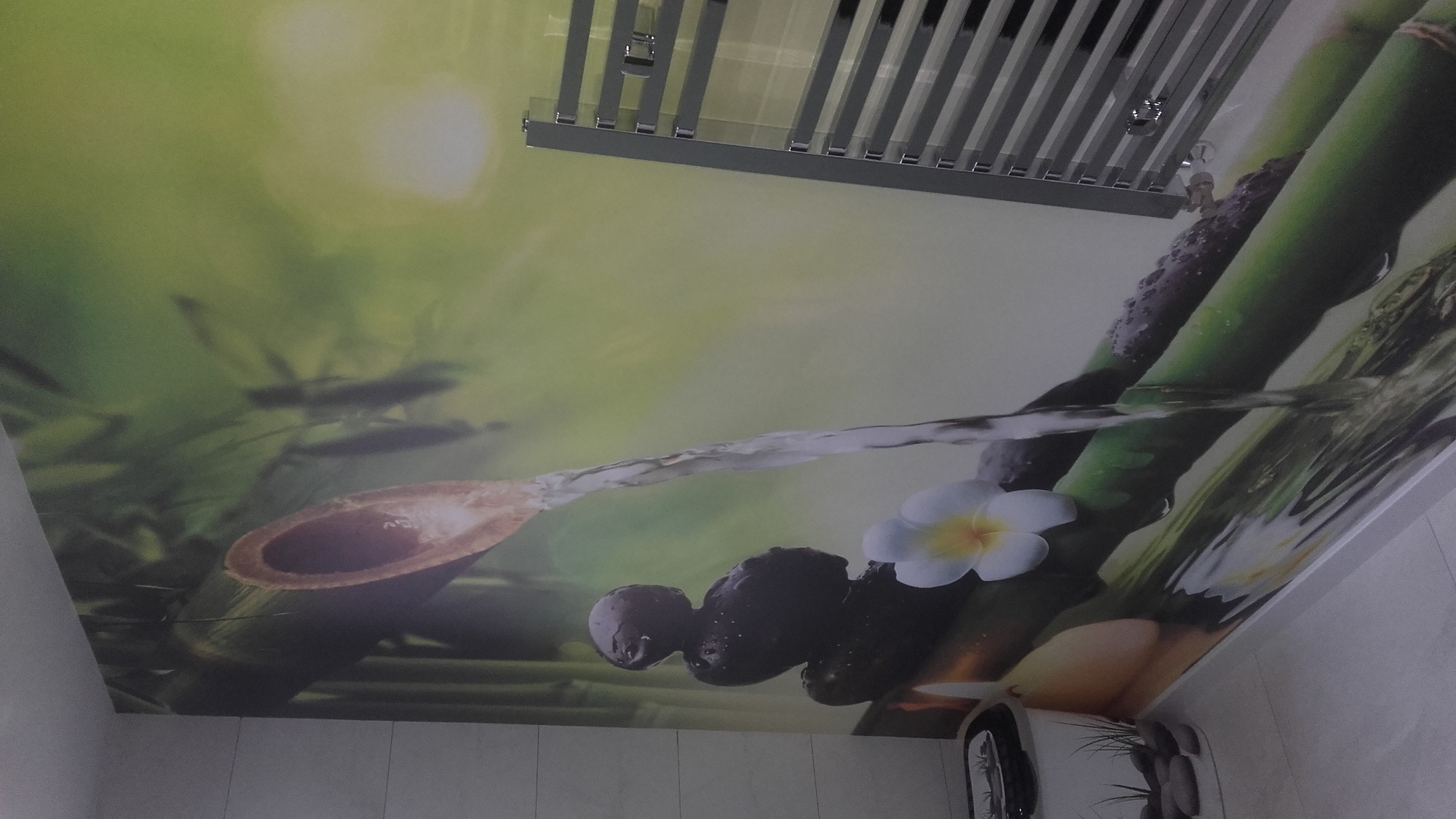 Sufit napinany z motywem bambusa, kamieni zen, kwiatów plumerii i odbiciem wody, oświetlenie sufitowe w tle.