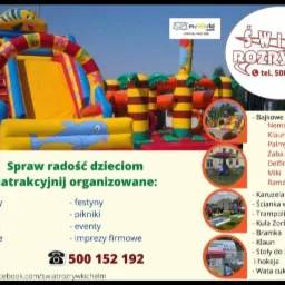 Kolorowy dmuchany zamek ze zjeżdżalnią w kształcie ryby, z logo firmy i ofertą atrakcji na tle zieleni.