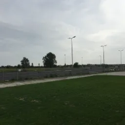 Teren przygotowany pod budowę: wyrównana działka z trawą, ogrodzenie panelowe i oświetlenie uliczne w tle, widoczne materiały budowlane.