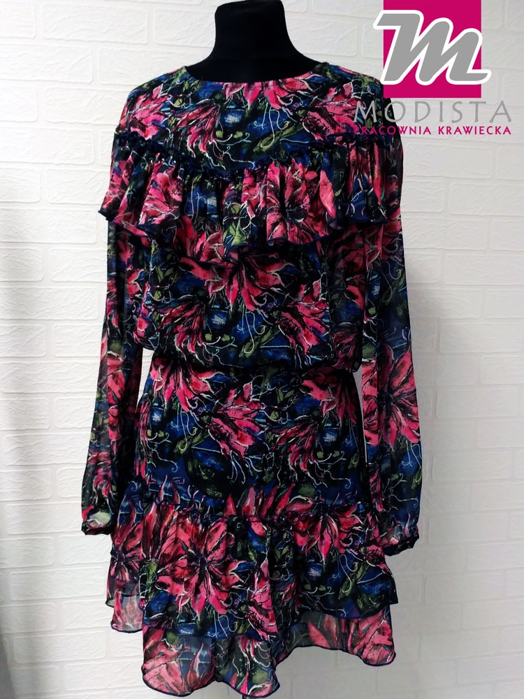 Sukienka z falbanami i kwiatowym wzorem na manekinie, logo pracowni krawieckiej w tle.