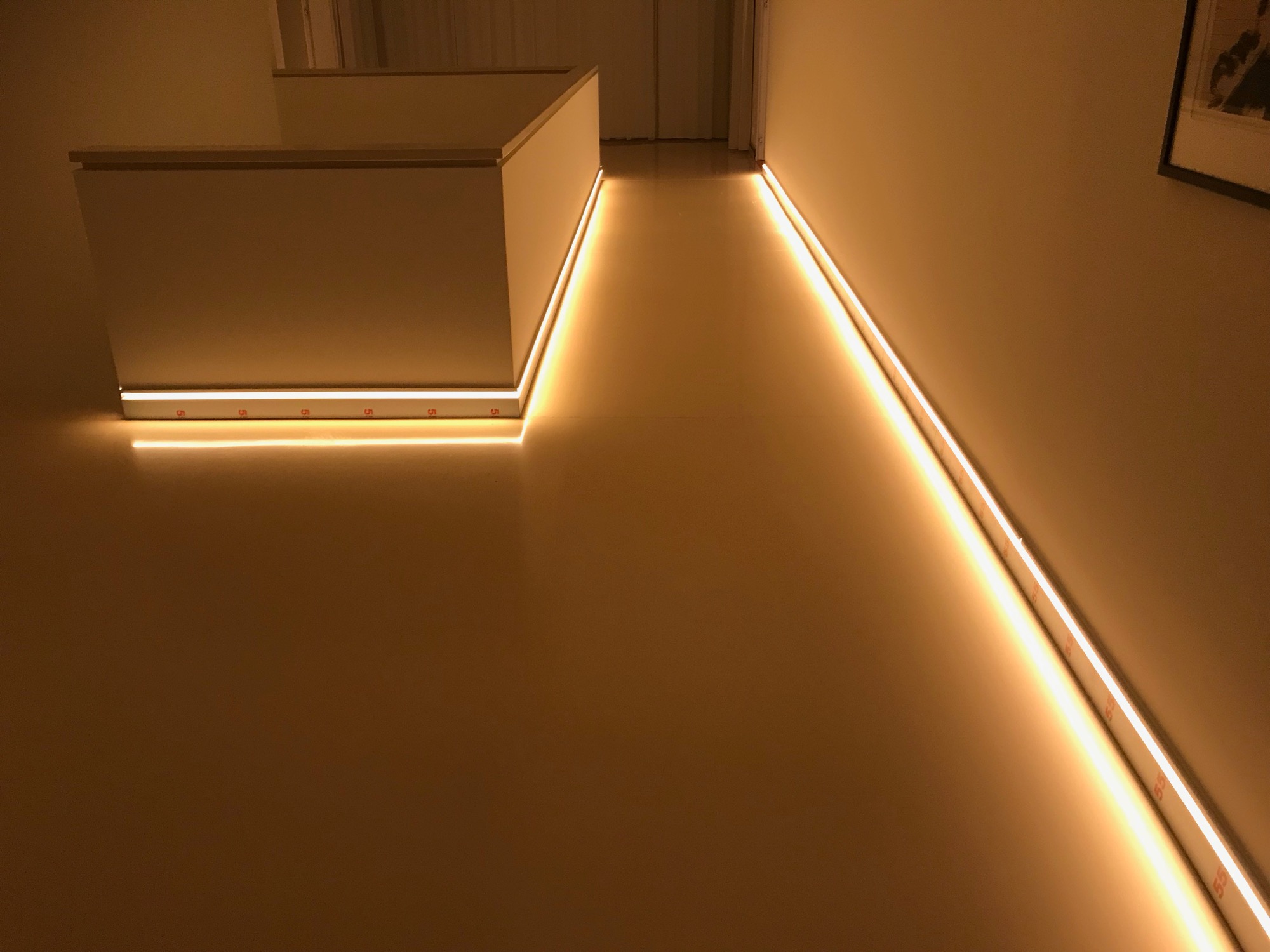 Nowoczesne oświetlenie LED zamontowane wzdłuż ściany i krawędzi schodów, tworzące ciepłą, nastrojową atmosferę w minimalistycznym wnętrzu.