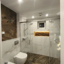 Nowoczesna łazienka z kabiną prysznicową typu walk-in, marmurowymi płytkami i akcentem w postaci podświetlanej wnęki. Bidet i toaleta podwieszana.