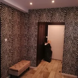 Korytarz z tapetą w zebrę, beżową pufą i czarnym workiem na śmieci w rogu