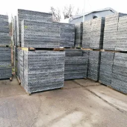 Stosy metalowych szalunków budowlanych ułożone na paletach, widoczne otwory montażowe, teren zewnętrzny.