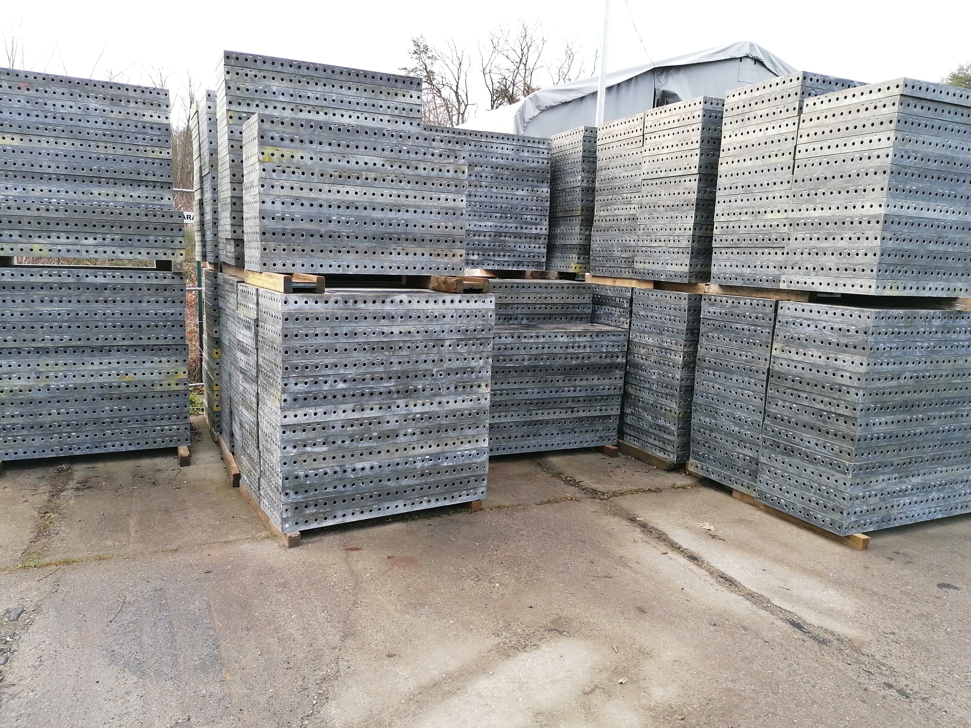 Stosy metalowych szalunków budowlanych ułożone na paletach, widoczne otwory montażowe, teren zewnętrzny.