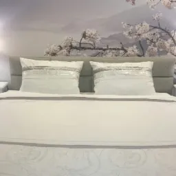 Sypialnia z łóżkiem małżeńskim, białymi meblami i fototapetą z motywem kwitnącej wiśni, oświetlona lampkami nocnymi.