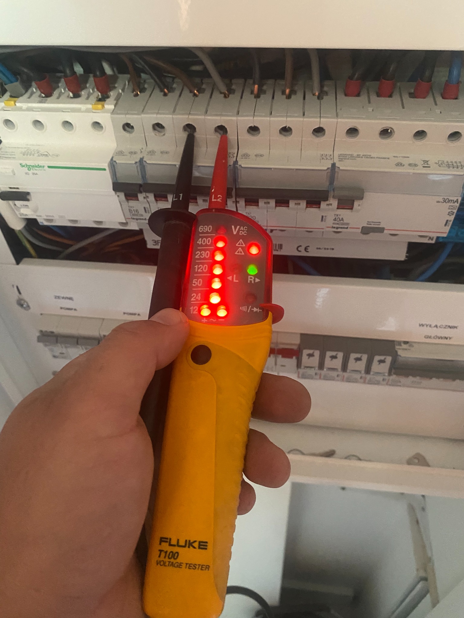 Sprawdzanie napięcia w rozdzielnicy elektrycznej za pomocą testera Fluke T100, widoczne wskaźniki napięcia L1 i L2 oraz diody sygnalizujące poziom napięcia