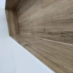 Wnęka w łazience wyłożona płytkami imitującymi drewno, kontrastująca z białymi płytkami na ścianach, ułożona poziomo, z delikatną fugą w kolorze zbliżonym do drewna.
