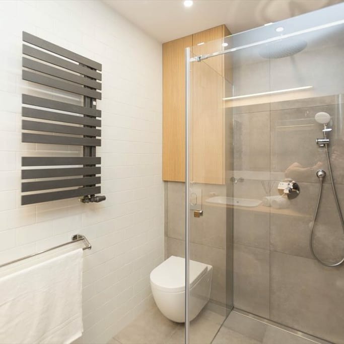 Nowoczesna łazienka z kabiną prysznicową typu walk-in, podwieszaną toaletą i grzejnikiem drabinkowym w kolorze grafitowym, biała ściana wyłożona cegiełkami.