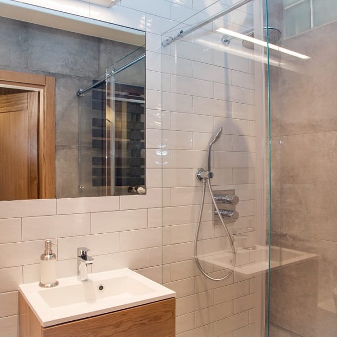 Nowoczesna łazienka z kabiną prysznicową typu walk-in, umywalką nablatową na drewnianej szafce i białymi płytkami imitującymi cegłę.
