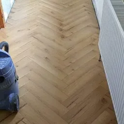 Ułożony parkiet w jodełkę, widoczny grzejnik, wiadro z farbą i odkurzacz, ściany przygotowane do malowania.