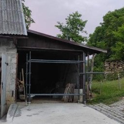 Paweł Koszyk - Przygotowanie do prac remontowych na zewnątrz budynku gospodarczego, widoczne rusztowanie i materiały budowlane.