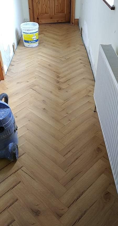 Ułożony parkiet w jodełkę, widoczny grzejnik, wiadro z farbą i odkurzacz, ściany przygotowane do malowania.