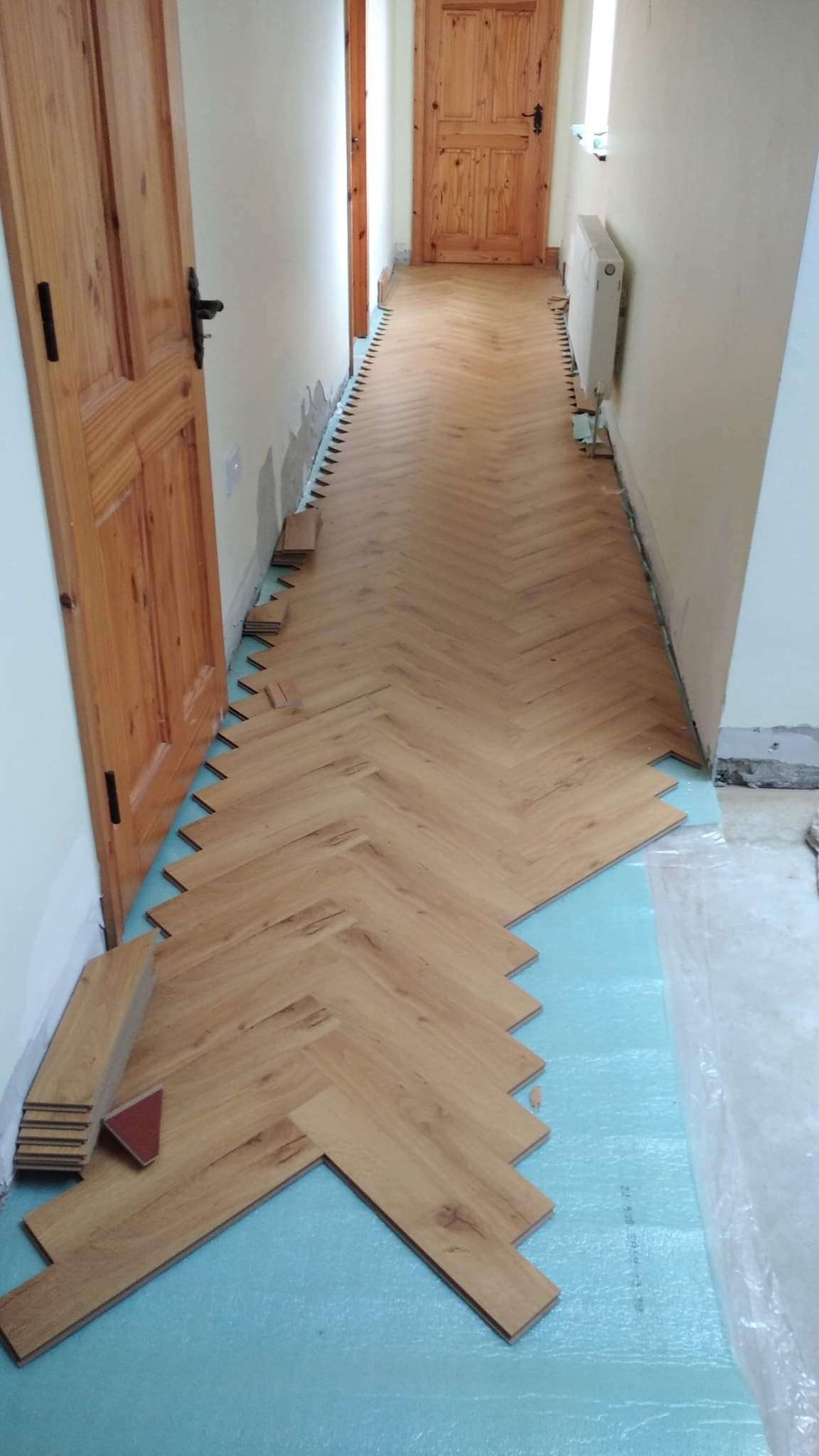 Układanie parkietu w jodełkę w korytarzu, widoczne docięte elementy oraz podkład z folii.