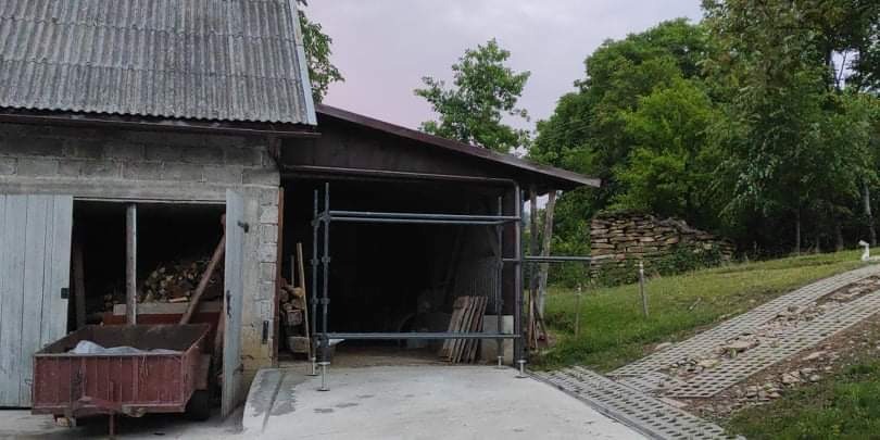 Przygotowanie do prac remontowych na zewnątrz budynku gospodarczego, widoczne rusztowanie i materiały budowlane.